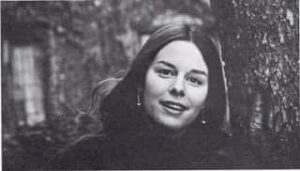 Portrait of Jane Mickelson as a young woman. She has long brown hair and is smiling and looking directly into the camera.